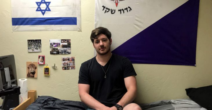 Former Israeli Defense Force soldier Yoni Wulf sits on his dorm bed at the University of Arizona in Tucson, Ariz. on October 10, 2019. The purple and white flag on his wall is the flag of his former platoon called the Shaked (acorn) platoon.